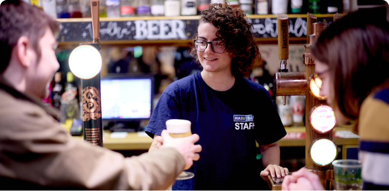 Student is serving a pint with a smile to customers